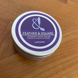 May include: A silver tin of lavender hand balm with the label "Feather & Square Rowers Hand Balm Created by Rowers for Rowers Lavender"