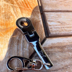 May include: A silver wrench keychain with a small loop for attaching to keys. The wrench has a small & symbol engraved on the handle.