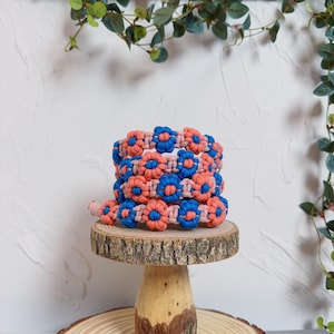 May include: A stack of colorful friendship bracelets with a pink and blue flower pattern. The bracelets are made with a macrame knotting technique.