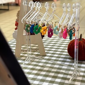 Peut inclure: Un présentoir en acrylique transparent avec des cintres miniatures tenant des porte-clés en forme de fleurs colorées. Les porte-clés sont de différentes couleurs, notamment rouge, orange, jaune, vert, bleu et violet.