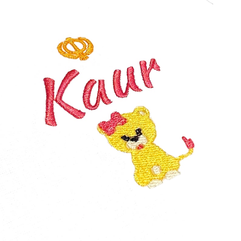 May include: Embroidered design featuring the name "Kaur" in pink lettering, a small yellow lion with a red bow, and a gold crown.