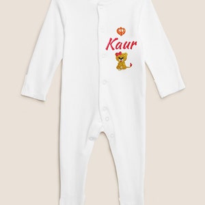 May include: White baby onesie with a pink lion and the name "Kaur" embroidered on the front.