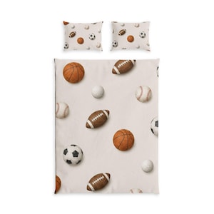 Op de afbeelding: Een beddengoedset bestaande uit een dekbedovertrek en twee kussenslopen, allemaal met een lichtbeige achtergrond voorzien van een patroon met diverse sportballen, waaronder basketballen, footballs, voetballen, honkballen en golfballen.