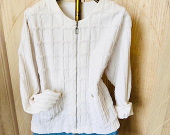 May include: White textured zip-up jacket with long sleeves and pockets, paired with blue denim shorts. The jacket has a grid-like pattern and a silver zipper. The shorts have a frayed hem.