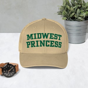 Puede incluir: Una gorra de béisbol de color beige con un diseño bordado en verde que dice "MIDWEST PRINCESS".