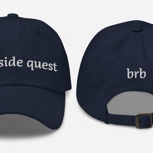 Puede incluir: Una gorra de béisbol azul marino con texto bordado en blanco. La parte delantera de la gorra dice "on a side quest" y la parte trasera dice "brb".