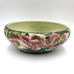 May include: A decorative ceramic bowl with a green interior and exterior. The exterior features raised relief floral designs in shades of pink, green, and white. The bowl has a wide, shallow shape.