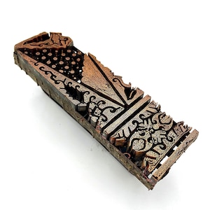May include: A rectangular copper block printing stamp featuring intricate, raised geometric and floral patterns. The metal surface displays a weathered, oxidized patina with detailed carvings designed for textile printing, showing a series of repeating motifs and fine lines across its entire length.