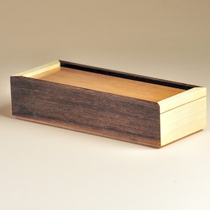May include: A rectangular wooden box with a lid. The box is made of two types of wood: dark brown on the sides and a lighter natural wood on the top and bottom. The box has clean lines and a minimalist design.