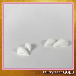 May include: Four white, glossy, pointed teeth arranged on a white surface. The teeth vary slightly in size and shape, with a smooth, reflective finish. The image is framed with a gold and pink border, with the text "TAILSQUARED GOLD" at the bottom.