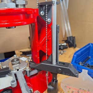 May include: A close-up of a reloading press with a black metal clamp attached to a silver rod. The clamp has a black lever and the text "SMALL" printed on it. A silver chain is attached to the clamp and the press.