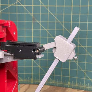 May include: A close-up of a black and gray reloading press with a gray lever arm. The lever arm is attached to the press with a screw.