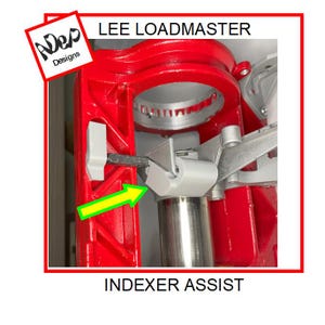 May include: A close-up of a red Lee Loadmaster reloading press with a gray plastic indexer assist. The indexer assist is a small, rectangular piece of plastic that helps to index the shell holder in the press.
