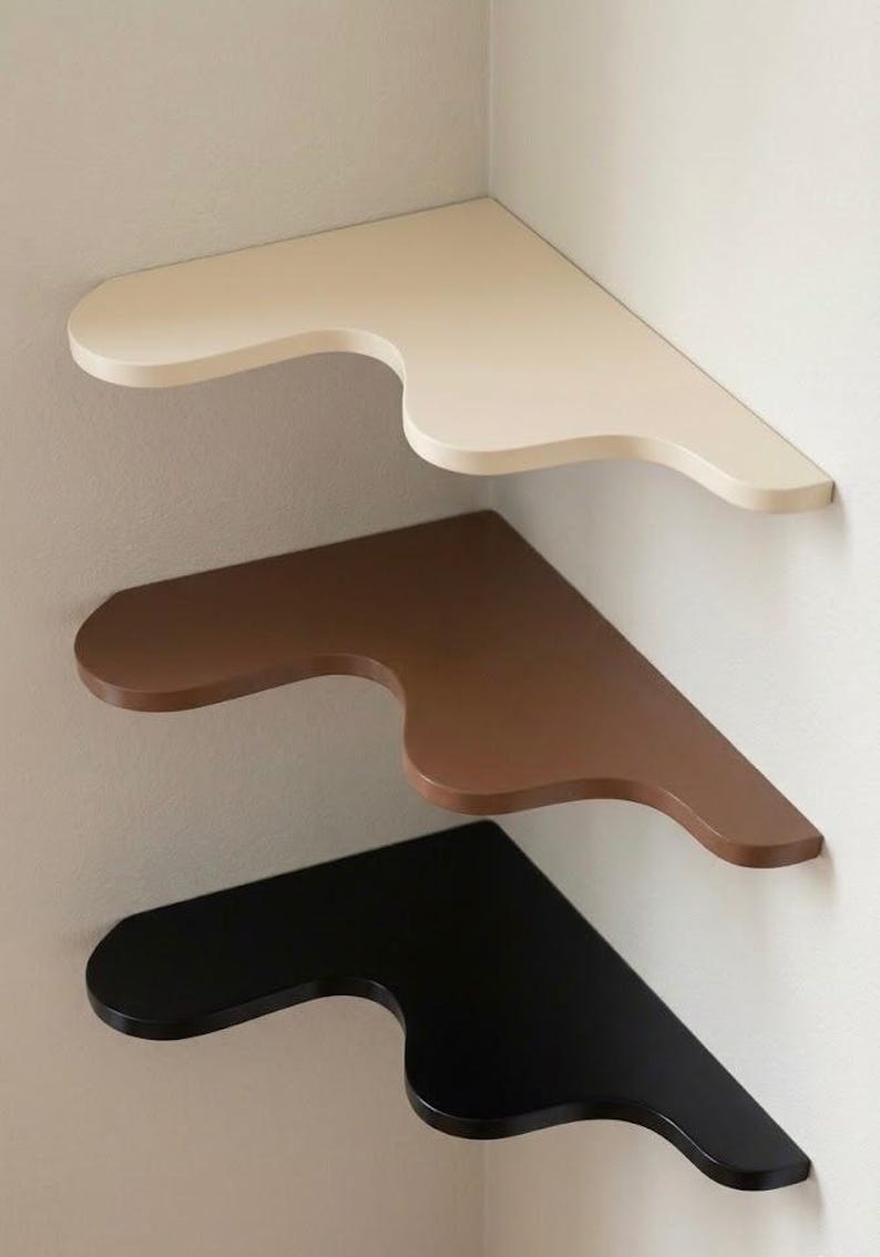 Puede incluir: Tres estanter&iacute;as de esquina en fila, cada una montada en una pared. La estanter&iacute;a superior es de color crema, la del medio es marr&oacute;n y la inferior es negra. Cada estanter&iacute;a tiene un dise&ntilde;o curvo &uacute;nico.