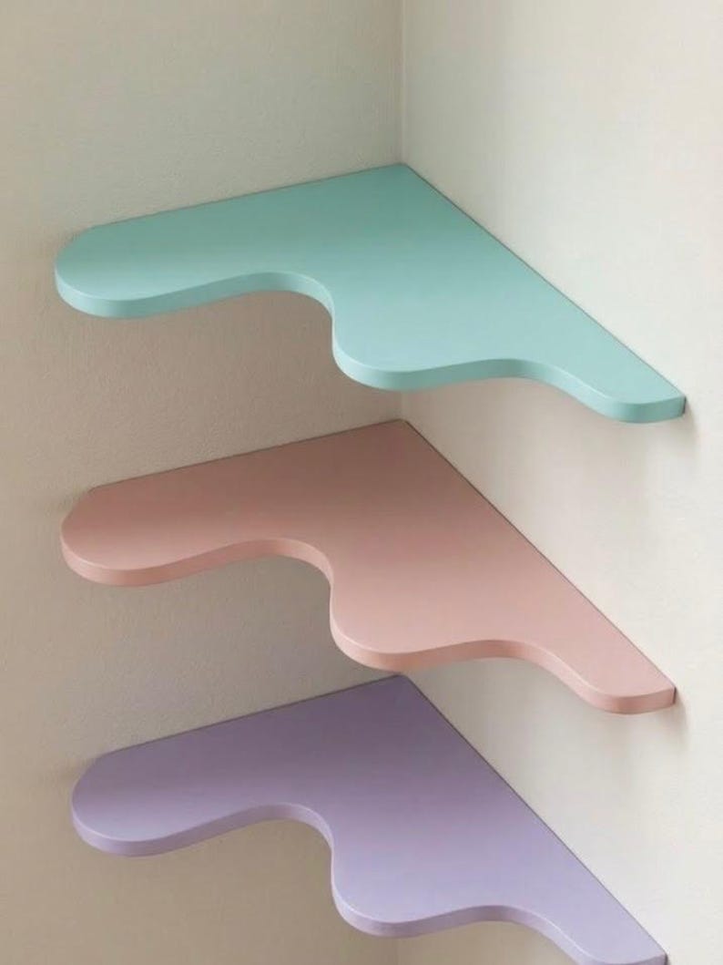 Puede incluir: Tres estanter&iacute;as de esquina en colores pastel: azul claro, rosa y lavanda. Cada estanter&iacute;a tiene un dise&ntilde;o curvo &uacute;nico en el borde frontal. Est&aacute;n montadas en una pared blanca, creando una est&eacute;tica moderna y minimalista.
