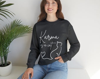 May include: A black sweatshirt with the text "Karma is a cat" in white lettering. A white outline of a cat is sitting to the right of the text. A white heart is below the text.