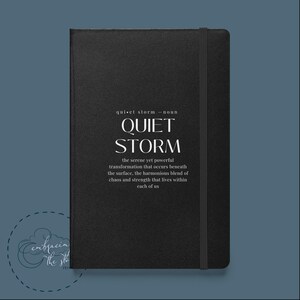 以下が含まれることがあります： 「quiet storm - noun the serene yet powerful transformation that occurs beneath the surface, the harmonious blend of chaos and strength that lives within each of us」という白い引用文が書かれた黒いノート