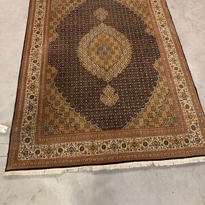 May include: A traditional Persian rug with a dark blue background and intricate gold and brown patterns. The rug has a white fringe border.