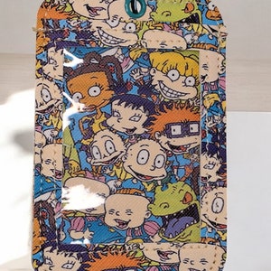 May include: Rectangular ID holder with a clear window and a silver key ring. The holder is covered in a colorful pattern of cartoon characters on a blue background. The characters have various expressions.