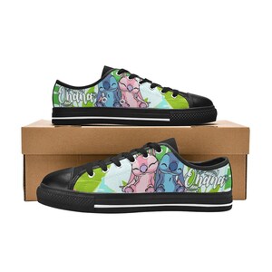 Puede incluir: Un par de zapatos de lona negros con un estampado floral verde, azul y rosa con Stitch y Angel de Lilo & Stitch. Los zapatos tienen cordones blancos y el texto "Ohana" est&aacute; impreso en el lateral.