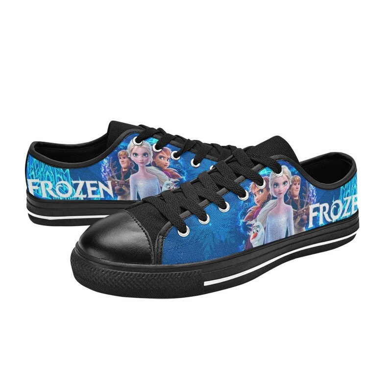 Puede incluir: Zapatillas bajas de lona negras con un estampado azul y blanco con personajes de la pel&iacute;cula Frozen. El estampado incluye las palabras "Frozen" y "Froze".