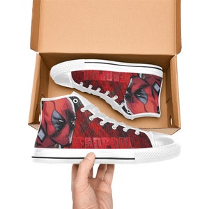 Può includere: Scarpe da ginnastica alte in tela bianca con un design Deadpool rosso e nero. Le scarpe presentano una grafica del viso di Deadpool e la parola "Deadpool" stampata sul lato.