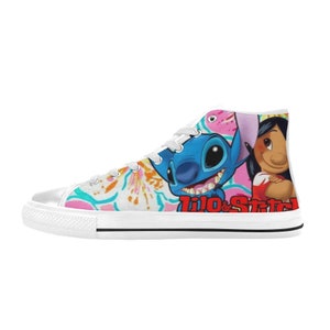 Op de afbeelding: Witte hoge canvas schoenen met een kleurrijke print met Stitch en Lilo uit de Disney-film Lilo & Stitch. De print bevat roze, blauwe, groene en gele bloemen. De tekst "Lilo & Stitch" is in rood gedrukt op de zijkant van de schoen.