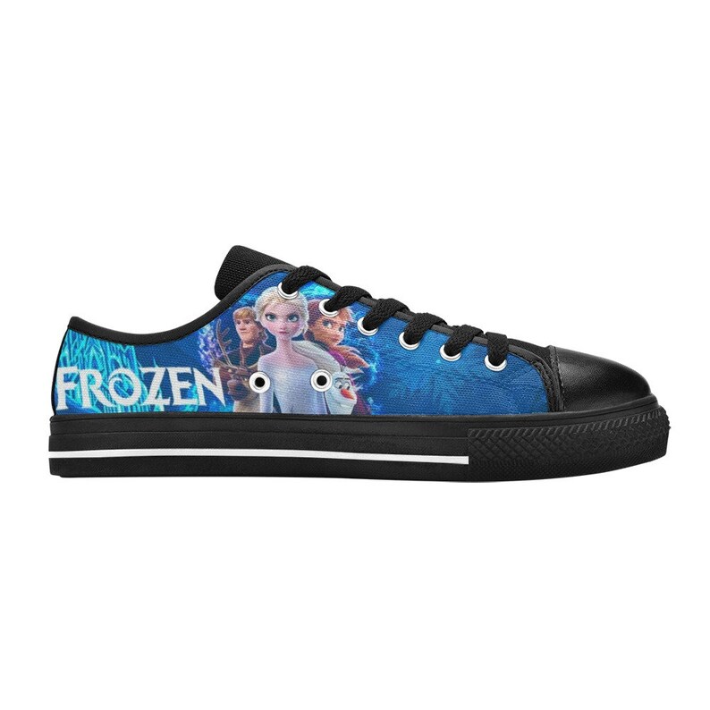 Puede incluir: Zapatillas bajas de lona negras con un estampado azul y blanco con los personajes de la pel&iacute;cula Frozen. El estampado incluye a Elsa, Anna, Kristoff y Olaf. La palabra "FROZEN" est&aacute; impresa en blanco en el lateral de la zapatilla.