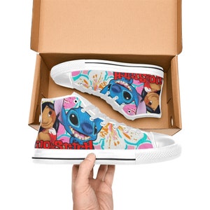 Op de afbeelding: Witte hoge canvas schoenen met een kleurrijke print met Stitch en Lilo uit de Disney-film Lilo & Stitch. De print bevat roze bloemen en de tekst "Lilo & Stitch".