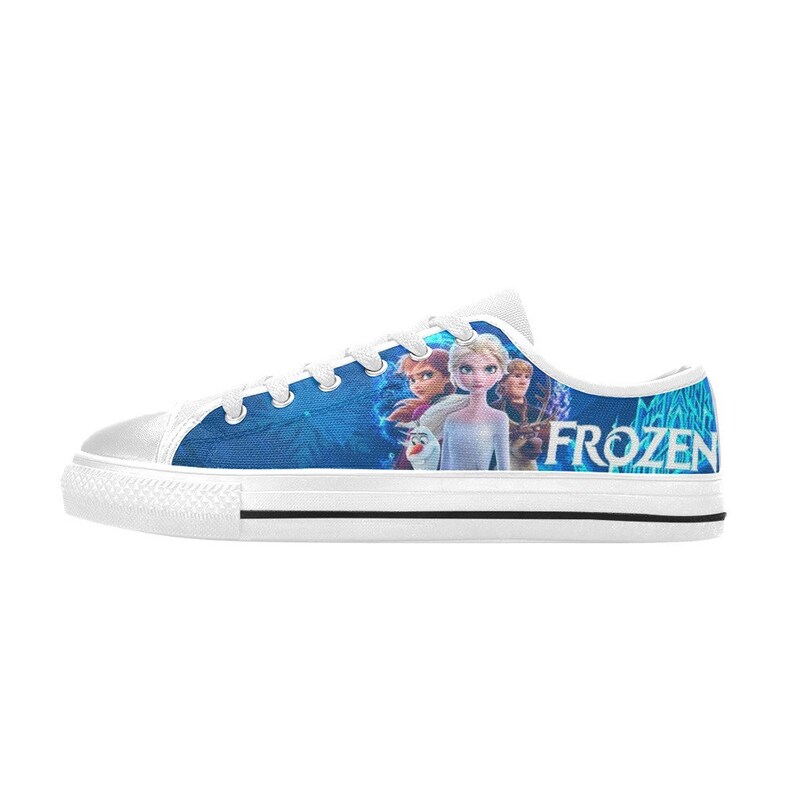 Puede incluir: Zapatillas bajas de lona blancas con un dise&ntilde;o azul y blanco con personajes de la pel&iacute;cula Frozen. El texto "FROZEN" est&aacute; impreso en el lateral del zapato.