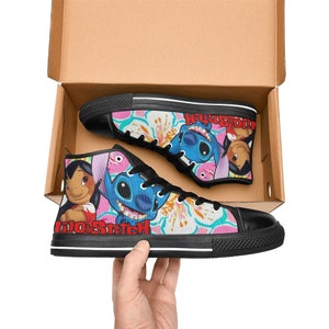Op de afbeelding: Een paar zwarte high-top canvas schoenen met een kleurrijke print met Stitch en Lilo uit de Disney-film Lilo & Stitch. De print bevat roze bloemen en de tekst "Lilo & Stitch".