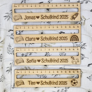 May include: Four wooden rulers, each measuring 15 cm, with engraved text and illustrations. The rulers are personalized with names like "Jonas" and "Clara", along with "Schulkind 2025" and various icons such as a rocket and a unicorn.