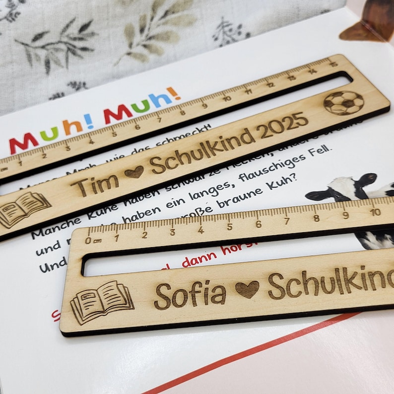 May include: Wooden rulers with engraved text and designs. One ruler has a soccer ball, another has a book icon, and all have measurement markings. The rulers are personalized with names and the text "Schulkind 2025".