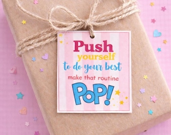 May include: A wrapped gift in brown paper, tied with twine and a bow. A rectangular tag with pink and white stripes reads "Push yourself to do your best, make that routine POP!" The background is pink with scattered star and heart confetti.