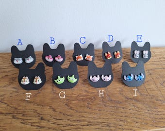 May include: Eight pairs of earrings displayed on black cardstock with letters A through I. The earrings feature various cartoon characters, including Stitch, a fox, a bunny, and a chipmunk.