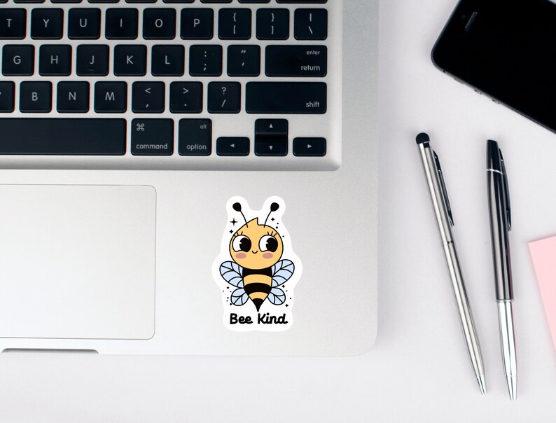 May include: A sticker with a cartoon bee with a yellow body, black stripes, and blue wings. The bee has a smiling face with eyelashes and a pink blush. The text "Bee Kind" is below the bee.