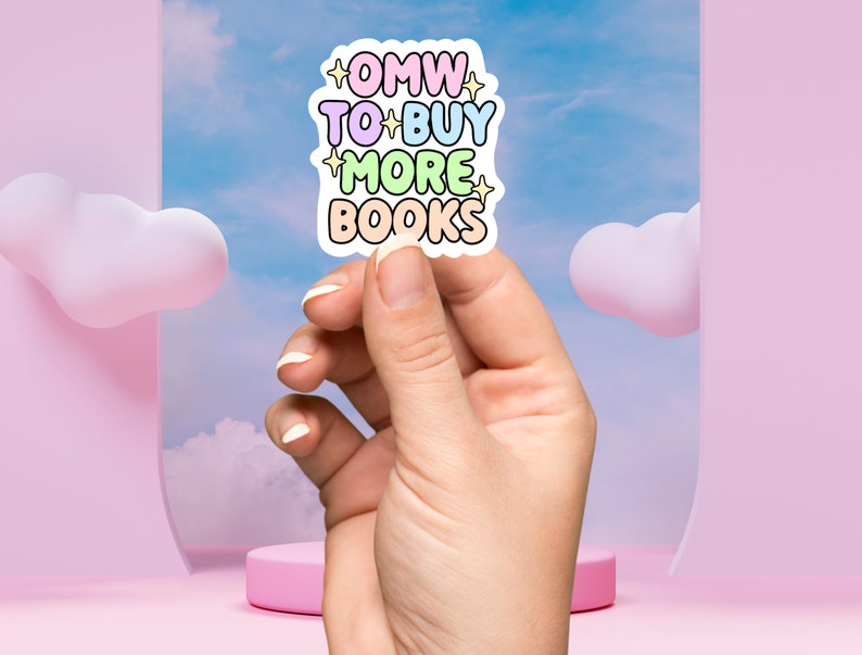 May include: A pastel pink, blue, yellow, and green sticker with the text "OMW TO BUY MORE BOOKS" with stars on either side of the text. The sticker is being held by a hand against a light blue background with pink clouds.