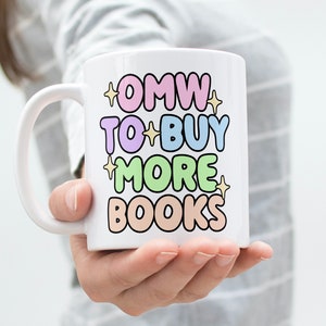 May include: White ceramic mug with a colourful design that says "OMW to buy more books".