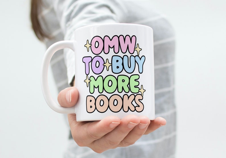May include: White ceramic mug with a colourful design that says "OMW to buy more books".
