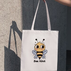 May include: White tote bag with a cartoon bee design and the text "Bee Kind".