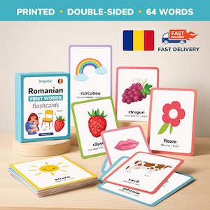 May include: A collection of Romanian first words flashcards with vibrant illustrations. The cards display images of a rainbow, grapes, a strawberry, a flower, a sun, a cow, and a lip. The box is labelled "Romanian First Words flashcards".