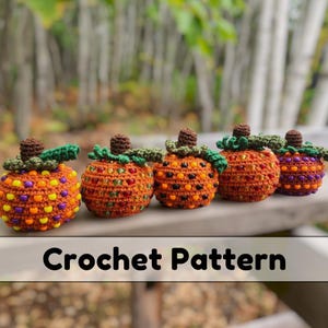 May include: Five handmade crochet pumpkins in a row, each with orange bodies adorned with colorful beads. They have brown stems and green leaf accents. The text "Crochet Pattern" is displayed at the bottom of the image.