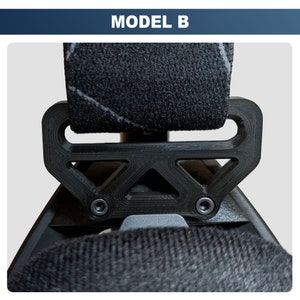 May include: Black plastic seat belt clip with a triangular pattern and two silver screws. The clip is attached to a black fabric seat belt.