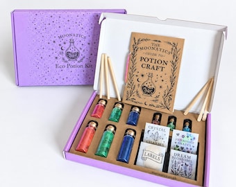 Puede incluir: Una caja morada Moonatics Eco Potion Kit que contiene una guía titulada The Moonatics Guide to Potion Craft, agitadores de madera, frascos de vidrio pequeños con polvos rojos, verdes y azules, y paquetes pequeños etiquetados como Crystal Charms, Friendship Shapes, Dream Blossoms y Labels.