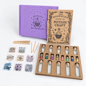 May include: A purple box labeled Moonatics Eco Potion Kit, a tan guide book titled The Moonatics Guide to Potion Craft, wooden stirrers, sticker sheets with text like Sun Threads and Crystal Charms, and a tray of small glass vials with corks.