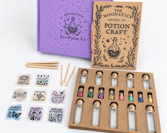 Puede incluir: Una caja morada etiquetada como Moonatics Eco Potion Kit, un libro guía color canela titulado The Moonatics Guide to Potion Craft, agitadores de madera, hojas de pegatinas con texto como Sun Threads y Crystal Charms, y viales de vidrio.