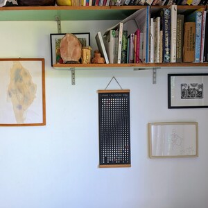 Hanging Moon Phase Lunar Calendar Print  on a household interior with a bookcase and other art