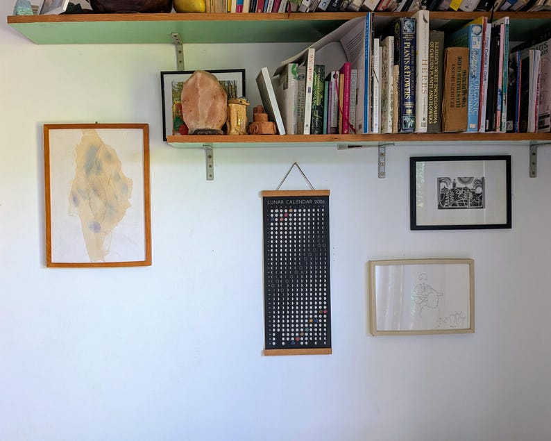 Hanging Moon Phase Lunar Calendar Print  on a household interior with a bookcase and other art