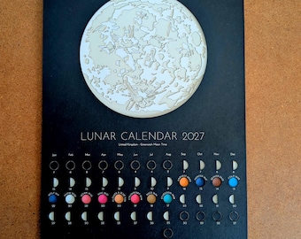 May include: A black 2027 lunar calendar featuring a large, detailed white moon illustration at the top. Below, the text reads LUNAR CALENDAR 2027 and United Kingdom - Greenwich Mean Time, followed by a grid of moon phases and colorful circular icons.