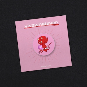 Puede incluir: Un pin de esmalte rosa y rojo con un diablo de dibujos animados que sostiene un corazón rosa con la palabra "ACAB" en él. El diablo sostiene un tenedor de heno y está de pie sobre un fondo rosa con un diseño de rayos de sol. El texto "vivawhatever" está impreso en negro en la parte superior del pin y "MADE IN THE USA" está impreso en negro en la parte inferior.
